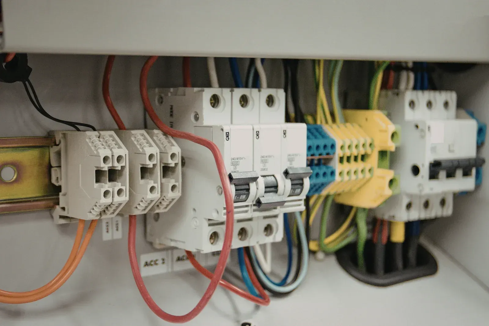 Interior view of an electrical control panel with circuit breakers and multicolored wiring on a DIN rail.