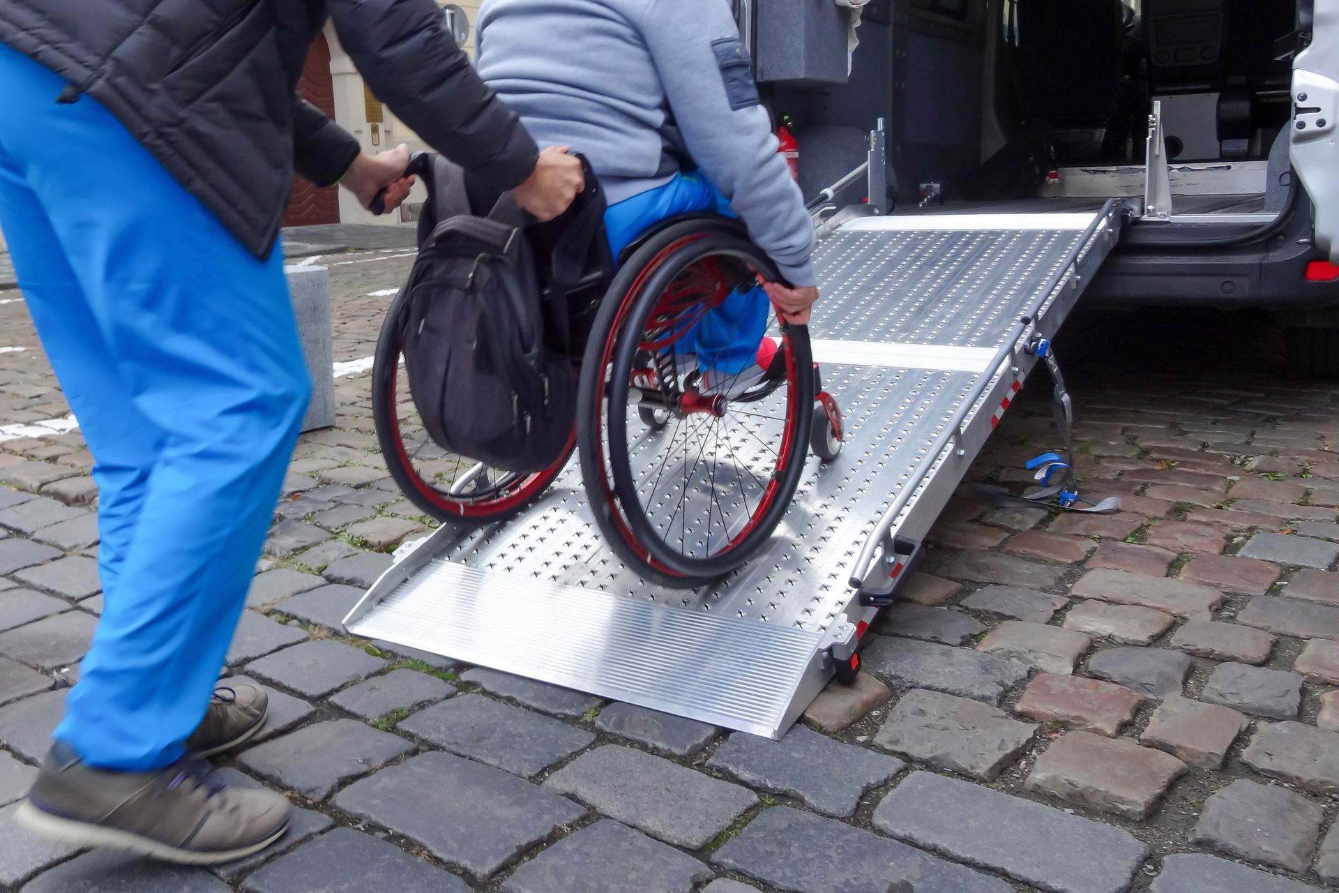 Medical transport caregiver assisting a male patient in a wheelchair onto a wheelchair accessible van using a ramp.