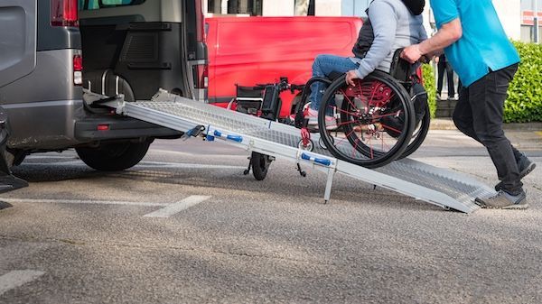 Professional staff member assisting a woman in a wheelchair onto a non-emergency medical transportation vehicle.