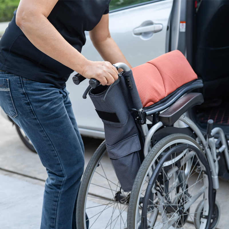 Caregiver folding up a wheelchair during a medical transportation transfer.