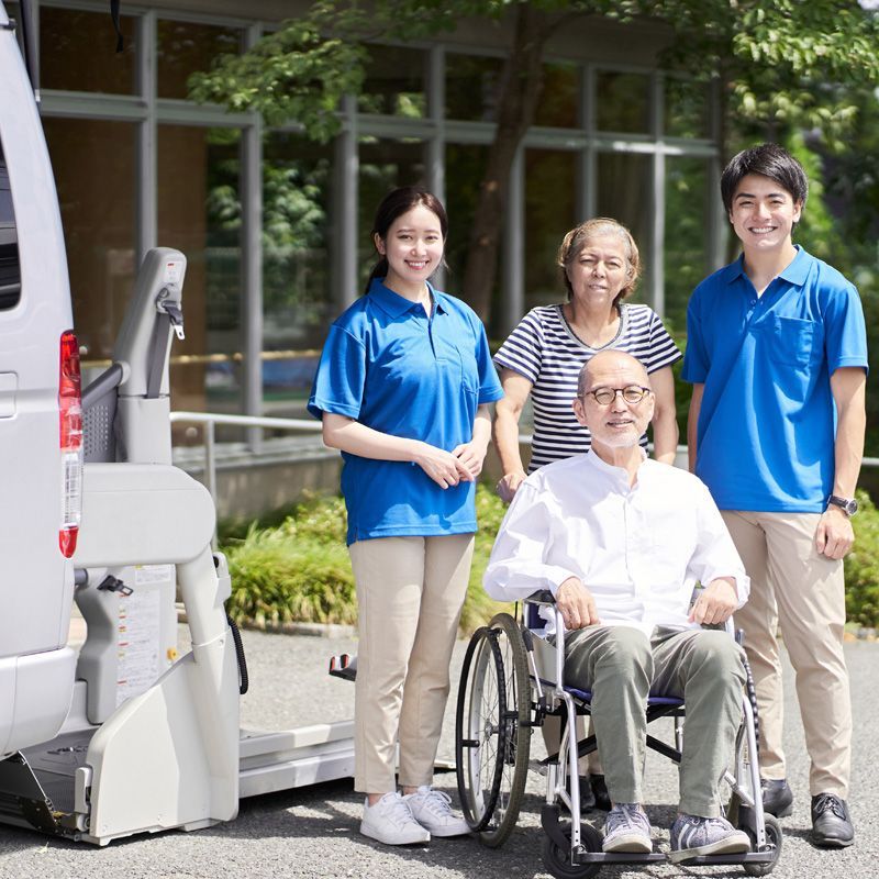 Senior man in a wheelchair with caregivers standing beside a wheelchair-accessible medical transportation van with a lift, representing safe and supportive non-emergency medical transportation.