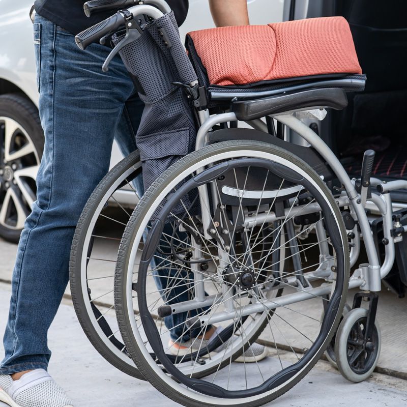 A foldable wheelchair is being loaded into a vehicle by a caregiver, illustrating accessible medical transportation and mobility support for patients.