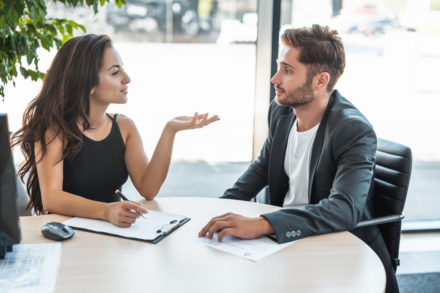 Woman gestures while speaking to a man at a table, documents present.