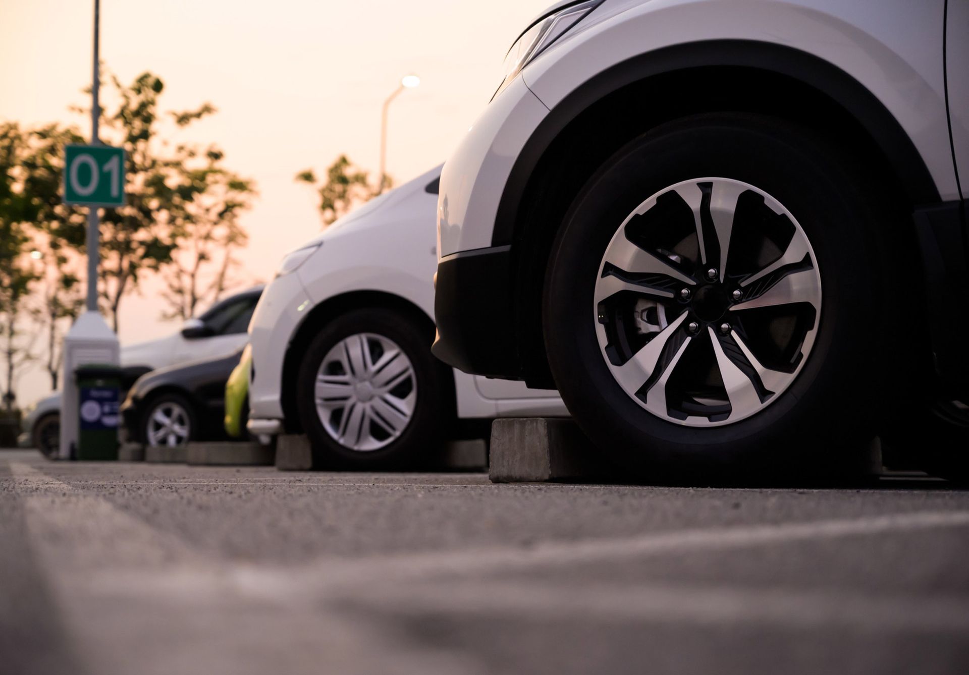 Cars parked in a parking lot, one with wheel close-up. Dusk setting.