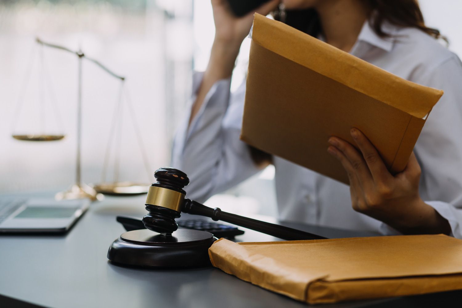 Gavel and scales on desk, person holding files and phone, legal setting.