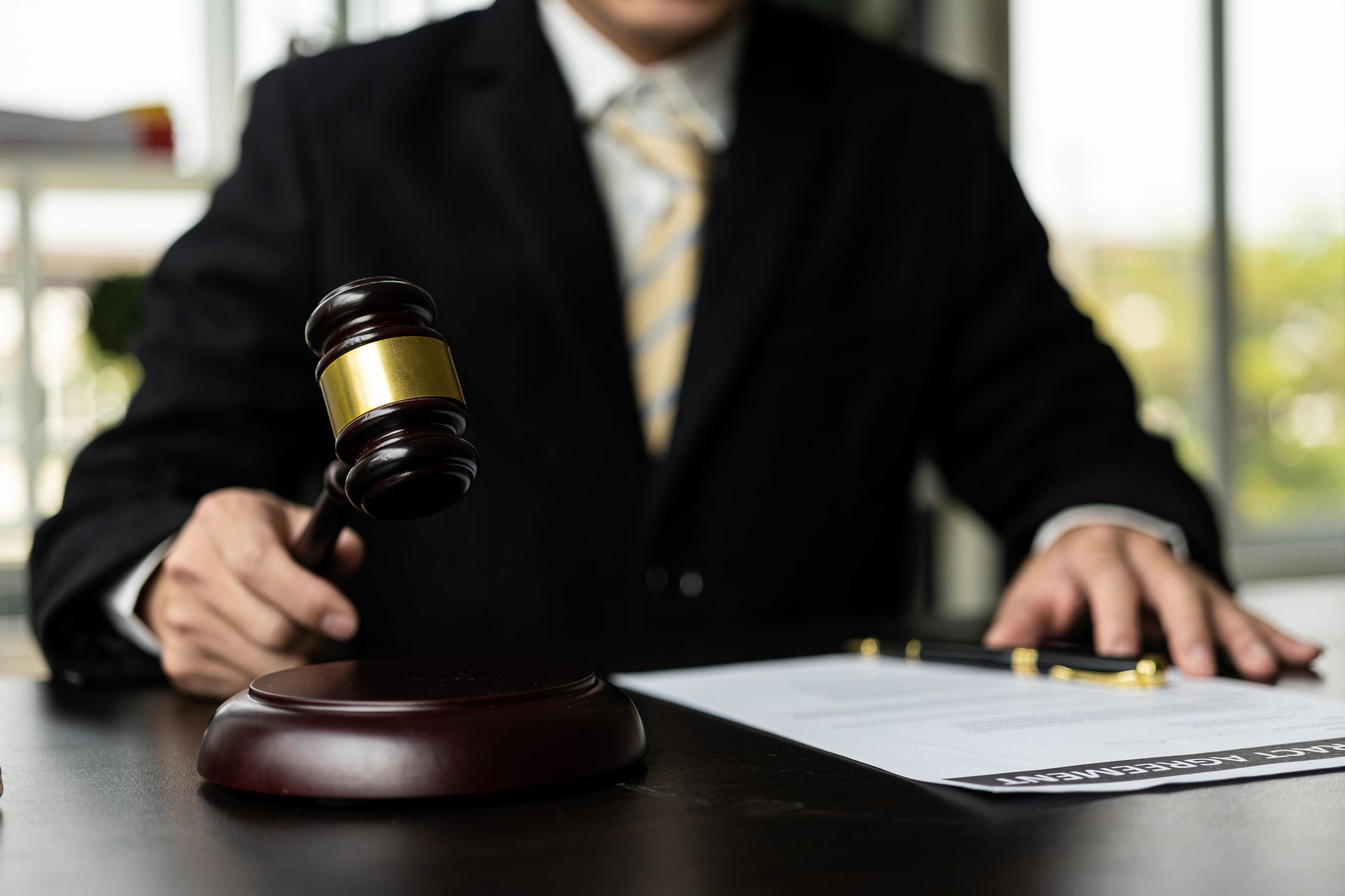 A person in a suit holding a gavel over a legal document on a desk.