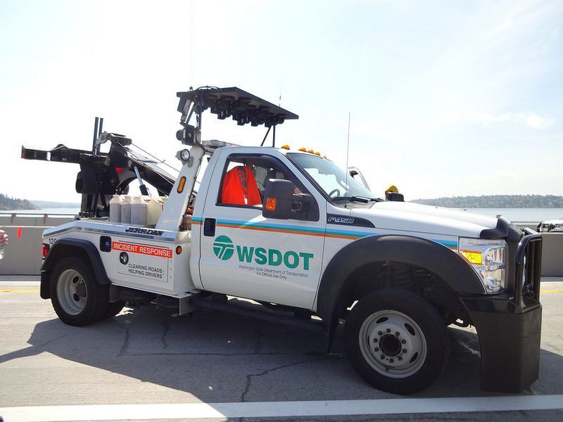 WSDOT tow truck on a bridge. White truck with green and blue accents. Boom and lights on top.