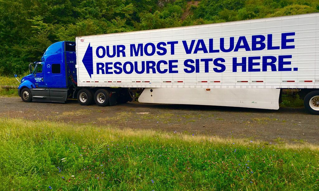 Blue semi-truck with trailer; white trailer reads 