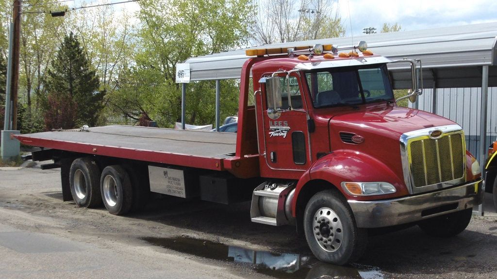 Red Peterbilt flatbed tow truck parked outdoors.
