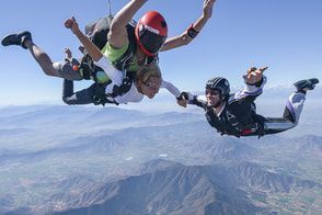 Two people in freefall, skydiving over a mountainous landscape.