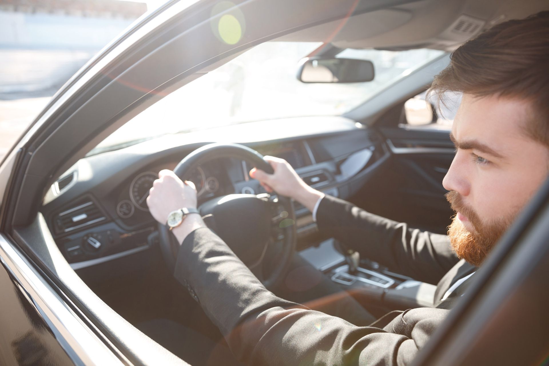 Man in suit driving a car, holding the steering wheel. Bright sunlight in the window.