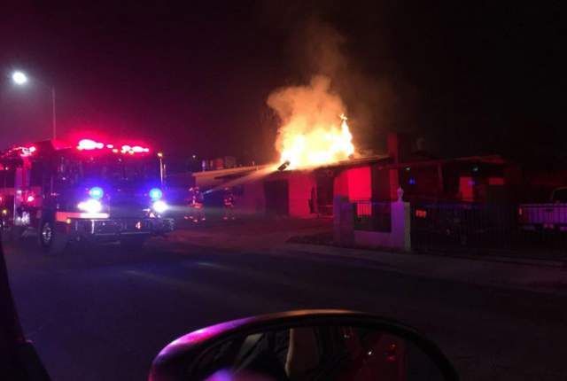 Firefighters battling a house fire at night. Flames and smoke billowing, fire truck with flashing lights.