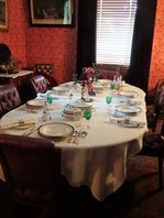 Formal dining table set for a meal in a room with patterned red wallpaper and a window with blinds.