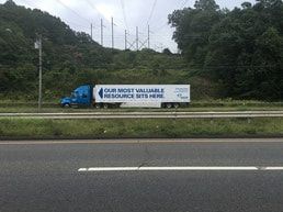 Blue semi-truck on highway, billboard reads 