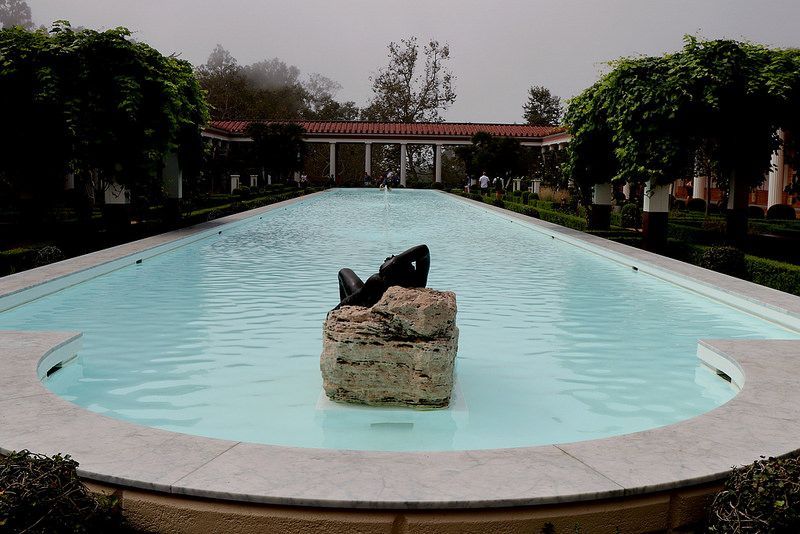 Long reflecting pool with sculpture; trees, colonnade in background.