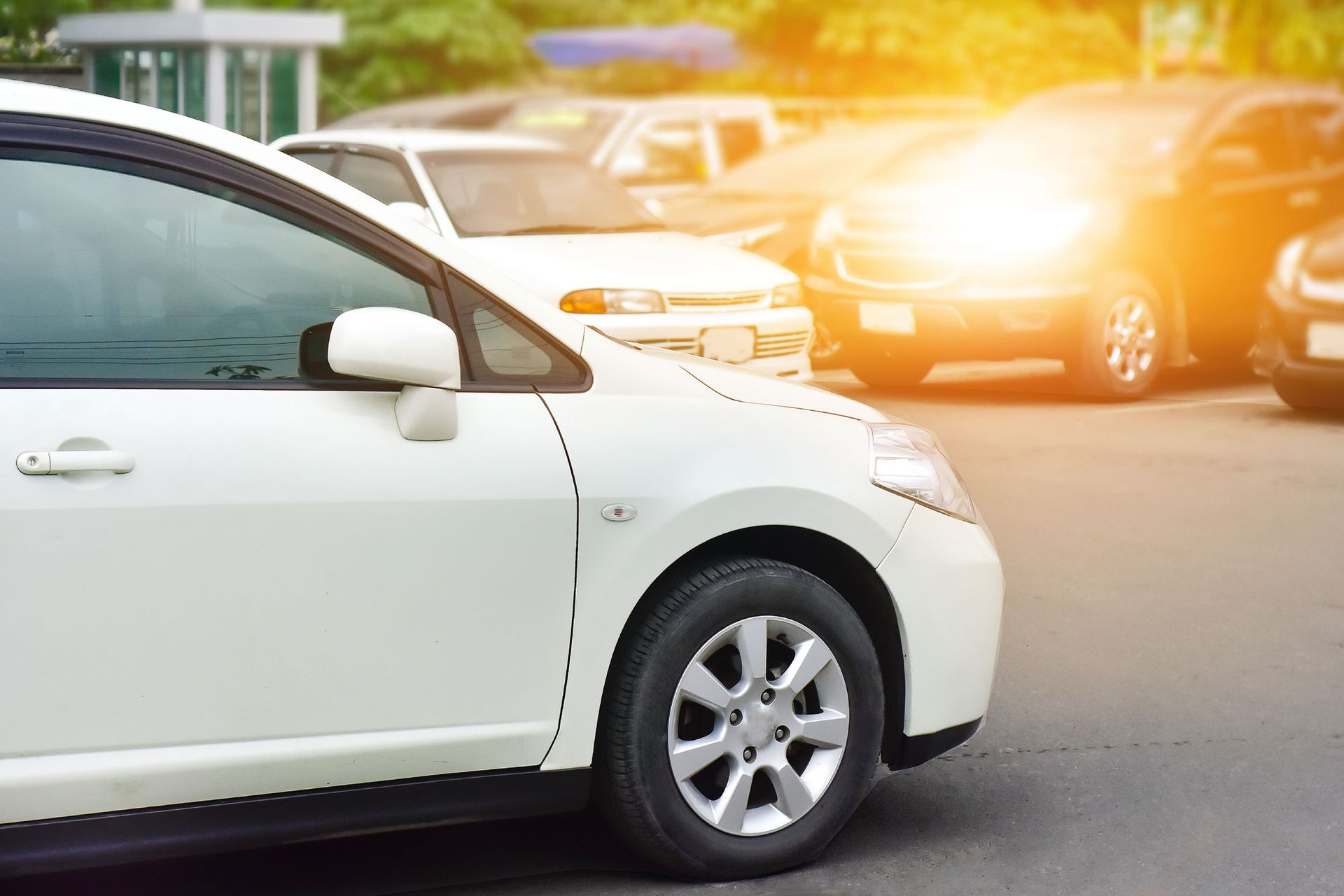 White car parked in a lot with other vehicles, sunlight in the background.