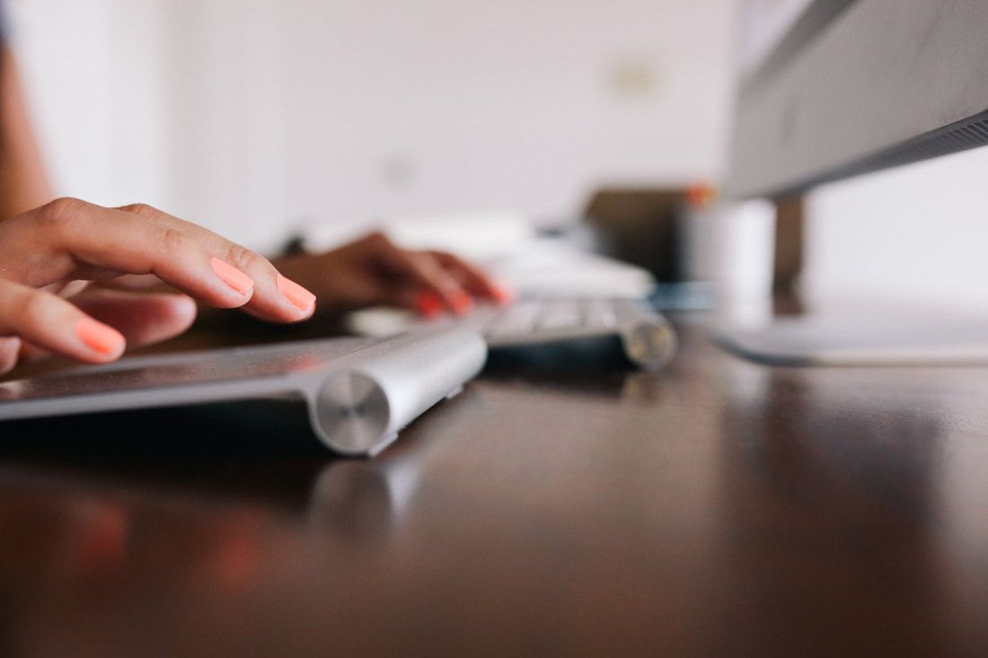 Person's hands typing on a keyboard, with a computer monitor in the background, set on a dark desk.