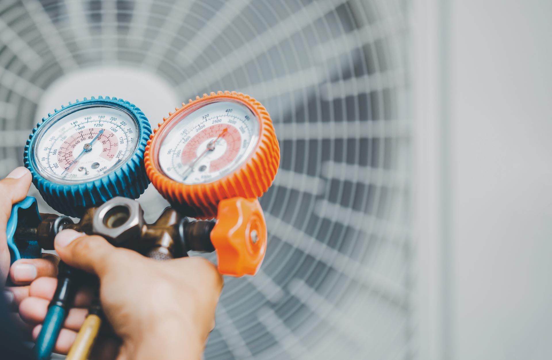 A person is holding two gauges in front of an air conditioner.