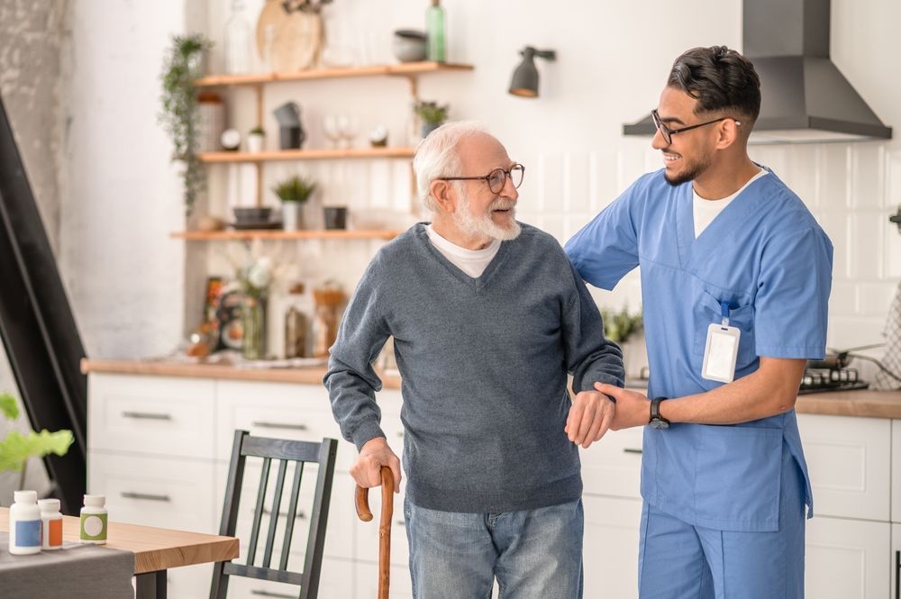 A nurse is helping an elderly man walk with a cane.