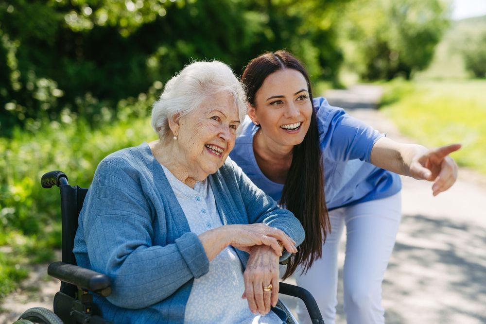 A woman is standing next to an elderly woman in a wheelchair.
