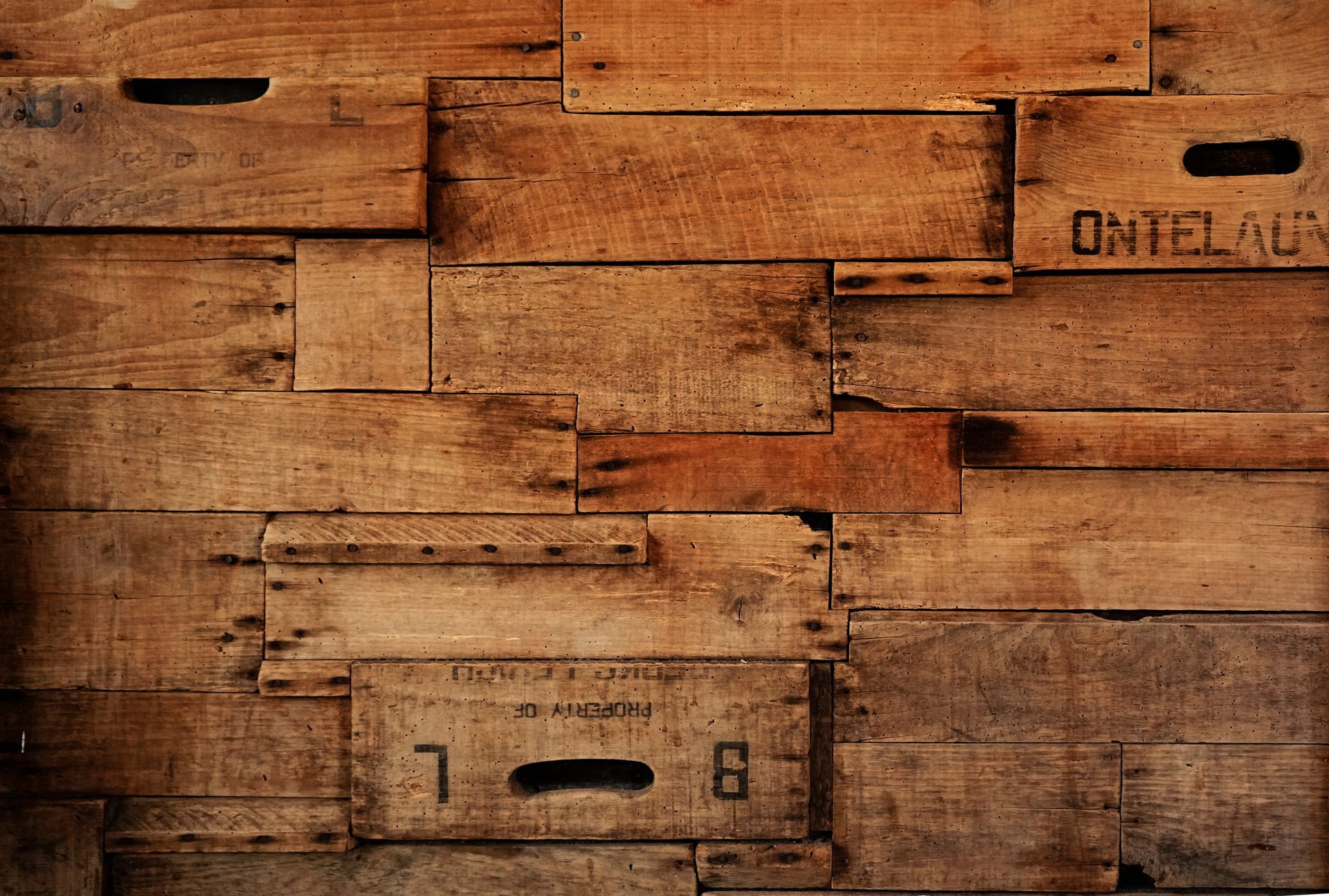 Stacked wooden crates in warm brown tones, with stenciled markings and cutout handles.
