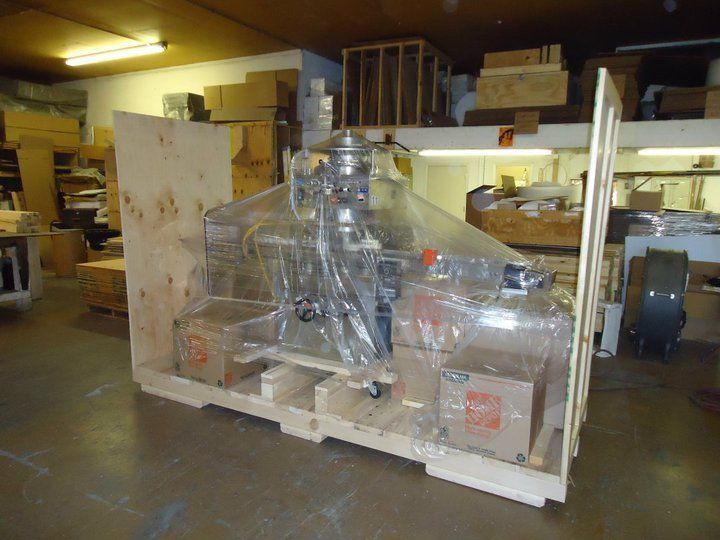 Plastic-wrapped industrial machine on a wooden pallet in a warehouse storage area