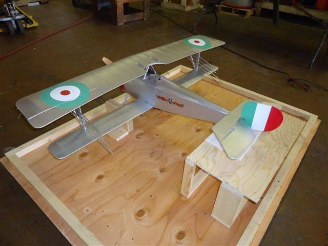 Model biplane on a wooden table, painted silver with green, white, and red wing markings.