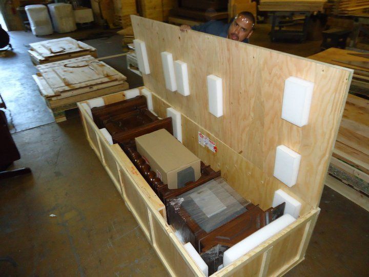 Open wooden crate with foam inserts and stacked components in a workshop warehouse