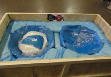 Two blue protective covers in a wooden crate, wrapped in plastic and foam padding
