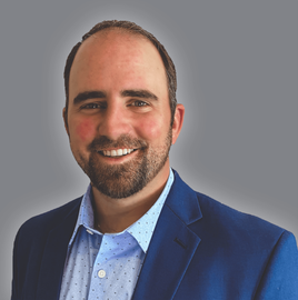 A man with a beard is wearing a blue suit and smiling