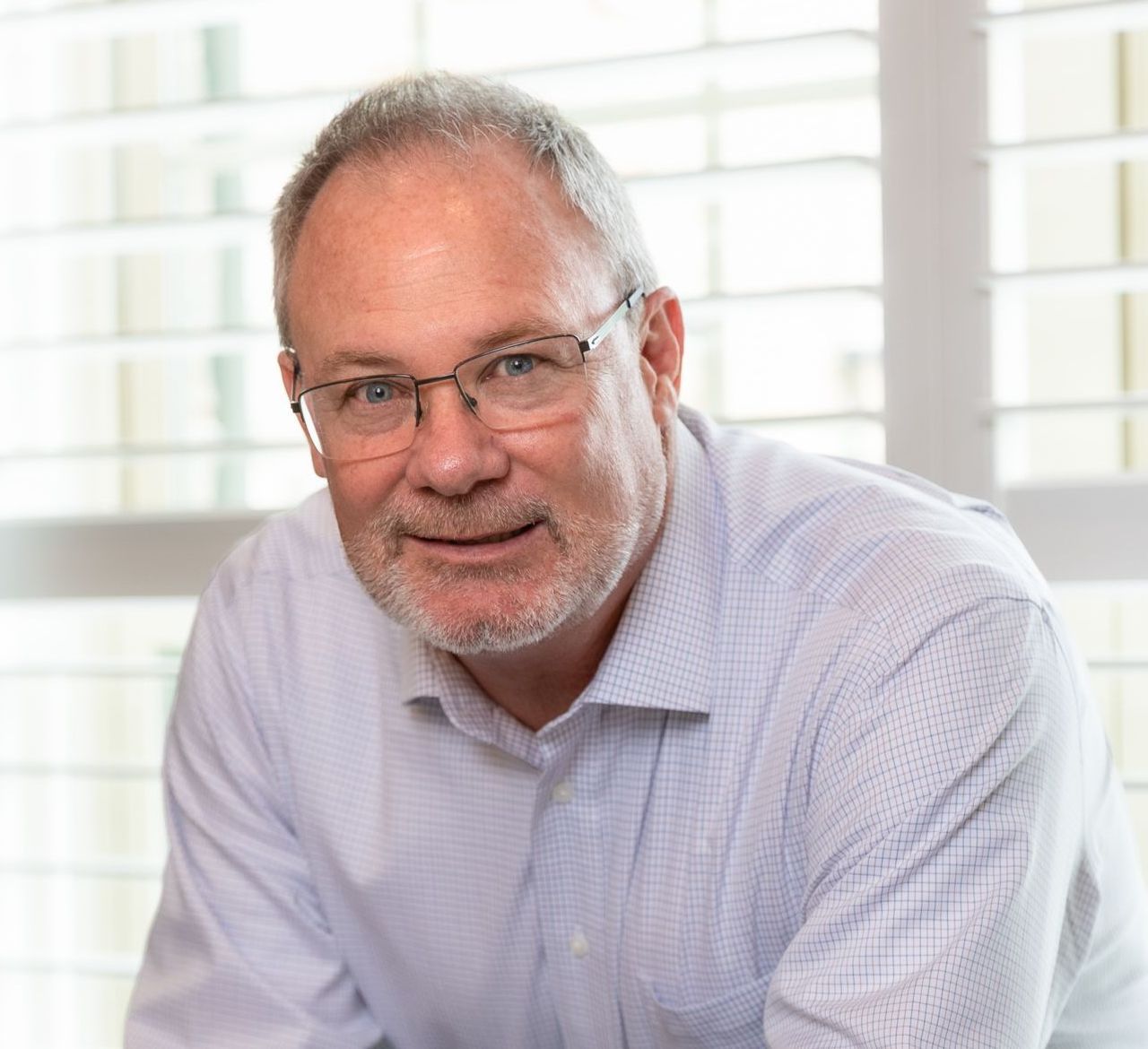 A man with glasses and a beard is sitting in front of a window.