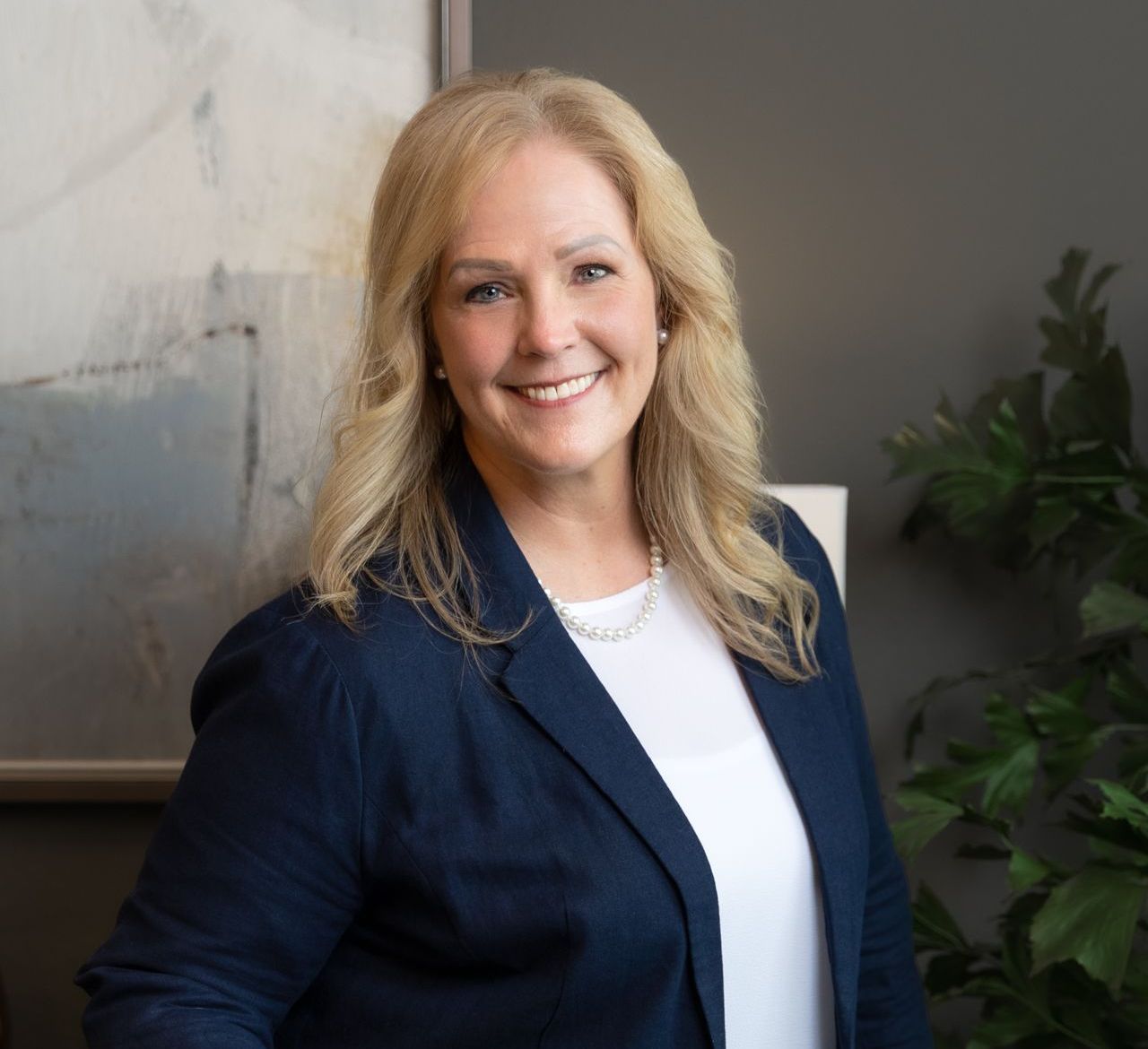 A woman in a blue jacket and white shirt is smiling for the camera.