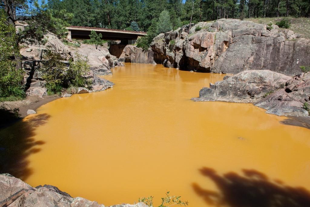 Orange-colored water fills a rock-walled body, with a bridge in the distance and trees in the background.