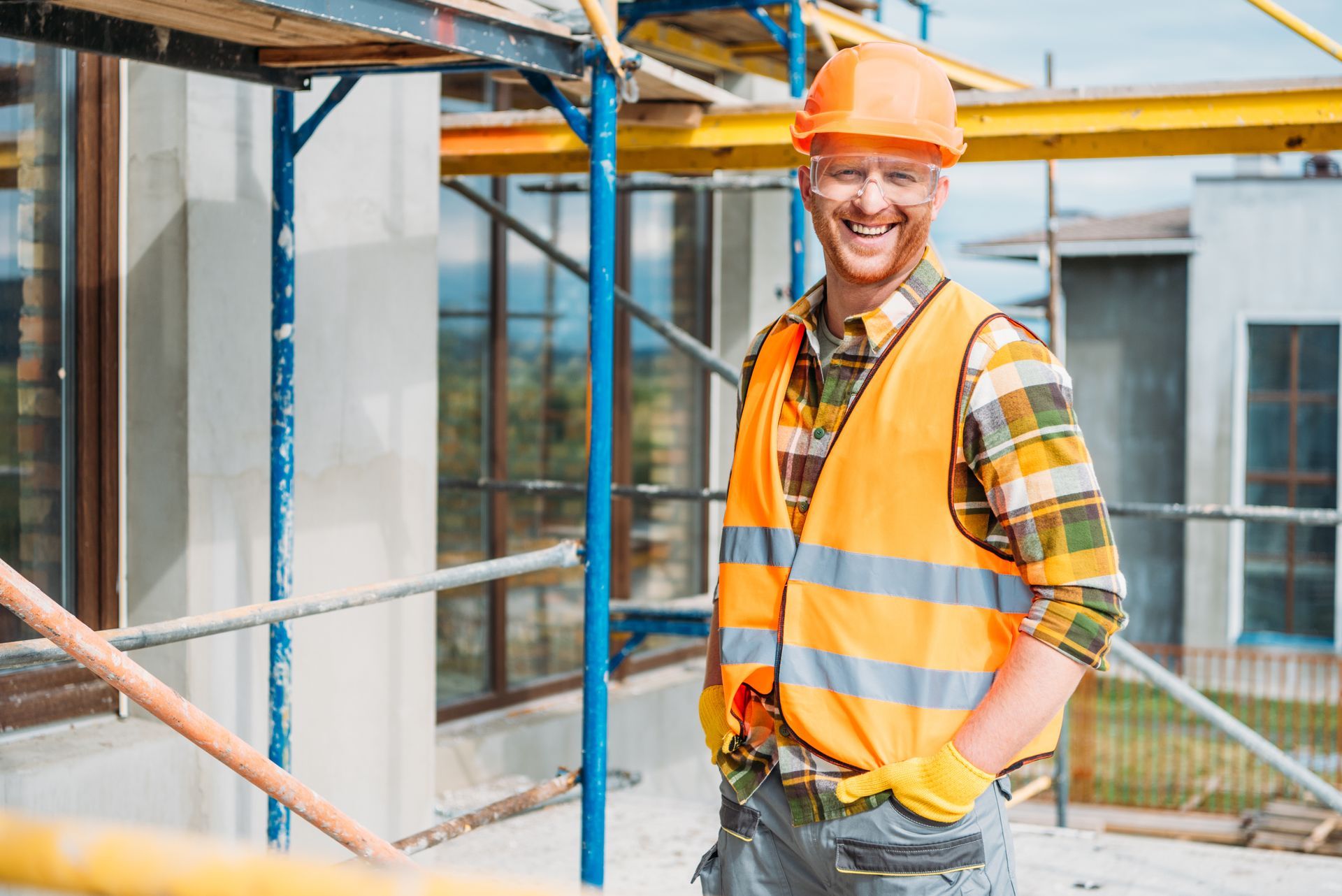 smiling builder in reflective vest and hard hat standing in front of scaffolding - demonstrating scaffolding safety