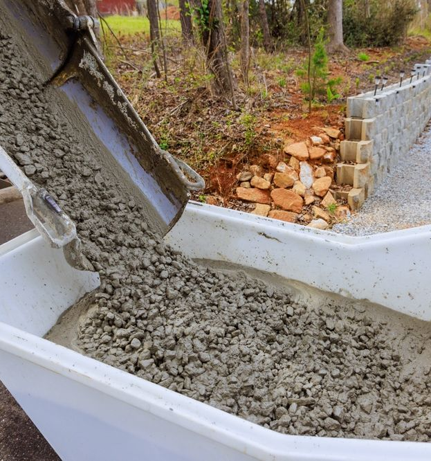 Concrete pouring from a truck chute into a white bin, near a stone wall.