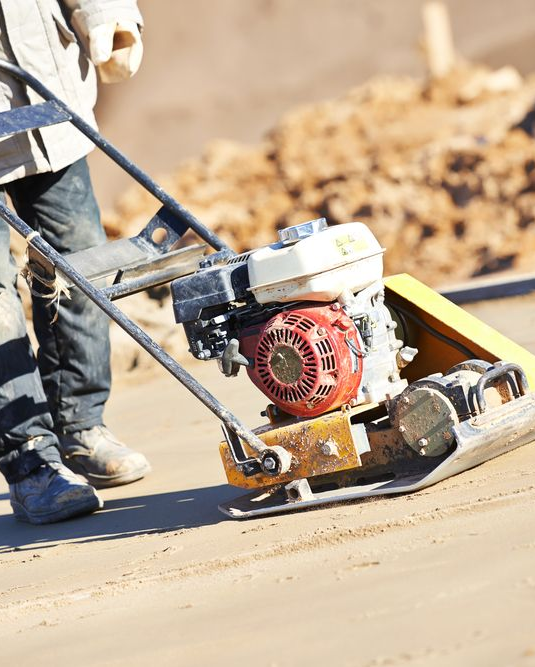 Person operating a plate compactor on a construction site, compacting the ground.