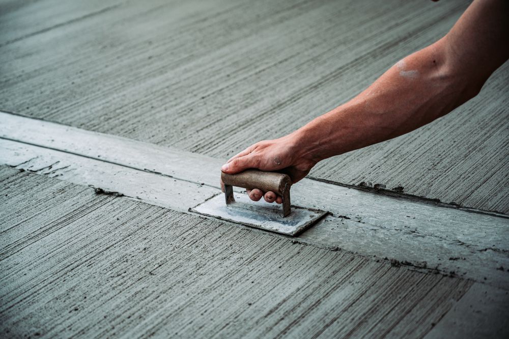 A person is using a trowel to spread concrete on the ground.