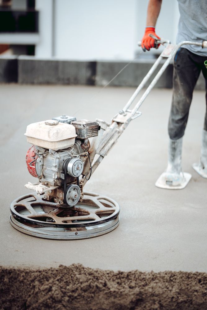 Person using a concrete power trowel to smooth a freshly poured concrete surface outdoors.