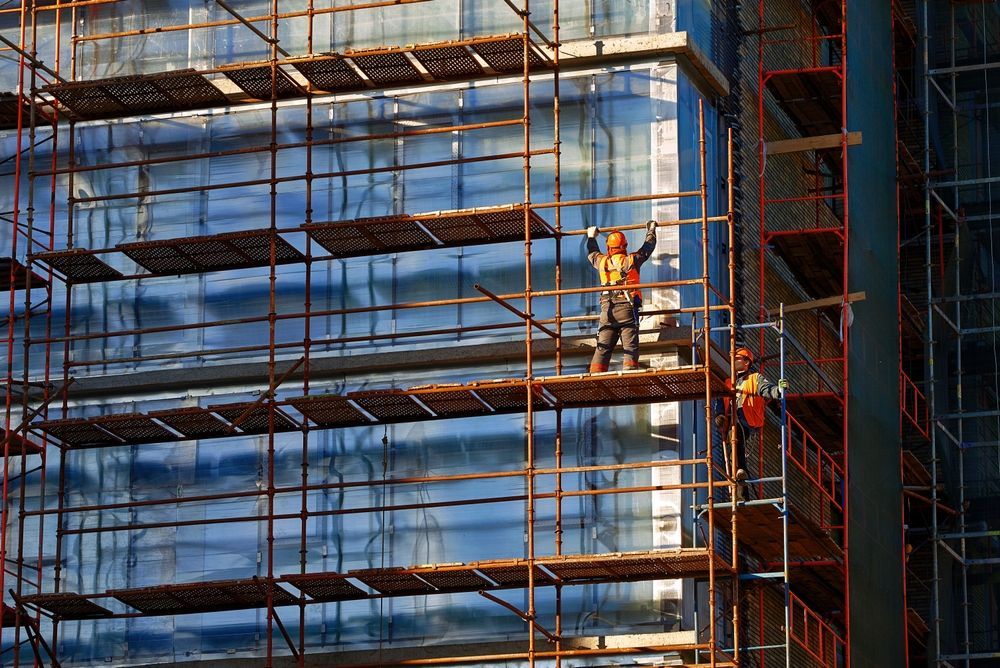 A construction worker is standing on a scaffolding on the side of a building.