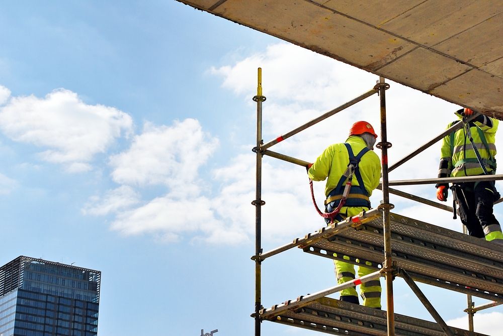 Two construction workers are standing on top of a scaffolding.