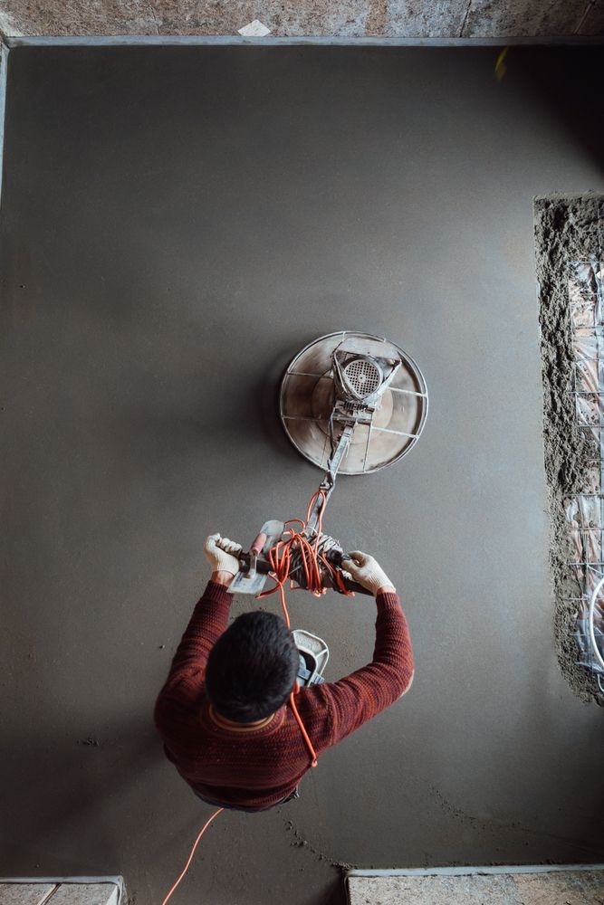 Concrete grinder on a gray concrete surface, tool with handle and wrapped orange cord.