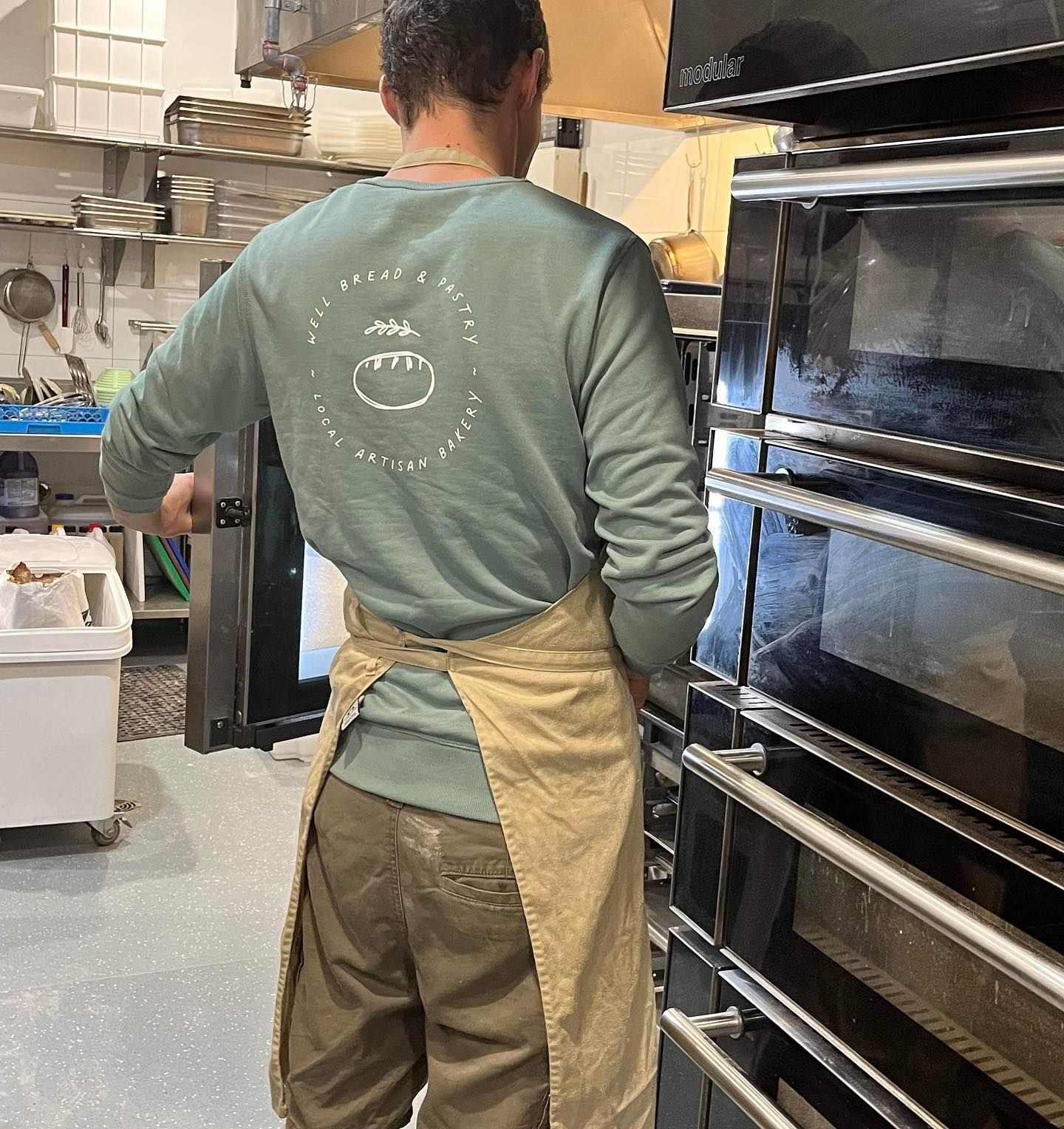 A man in an apron is standing in front of an oven