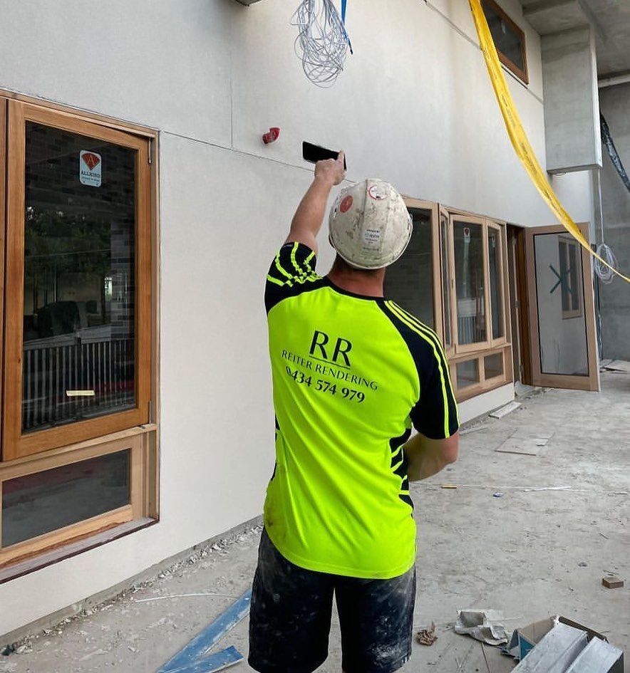 A man wearing a hat and sunglasses is standing in front of a brick wall.