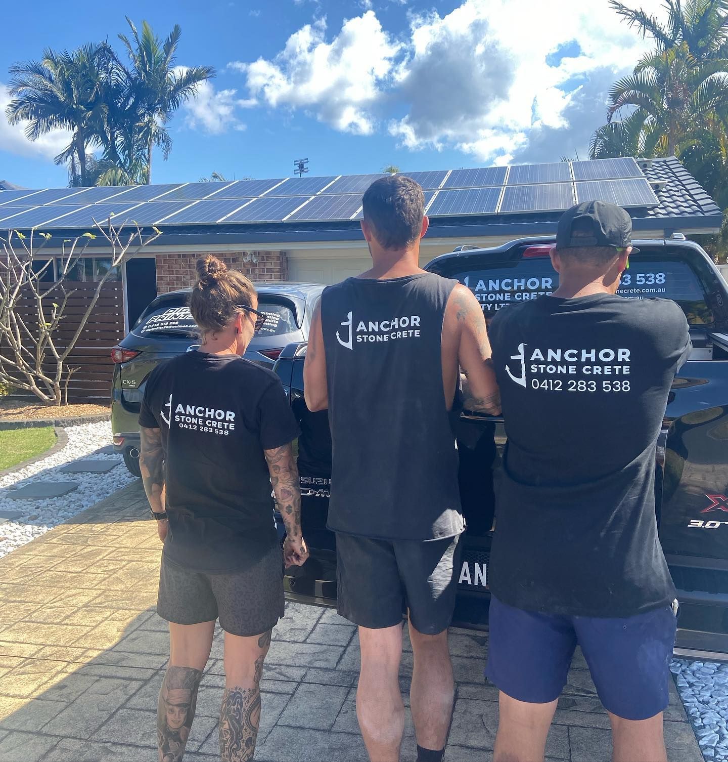 Three people wearing anchor shirts are standing in front of a truck