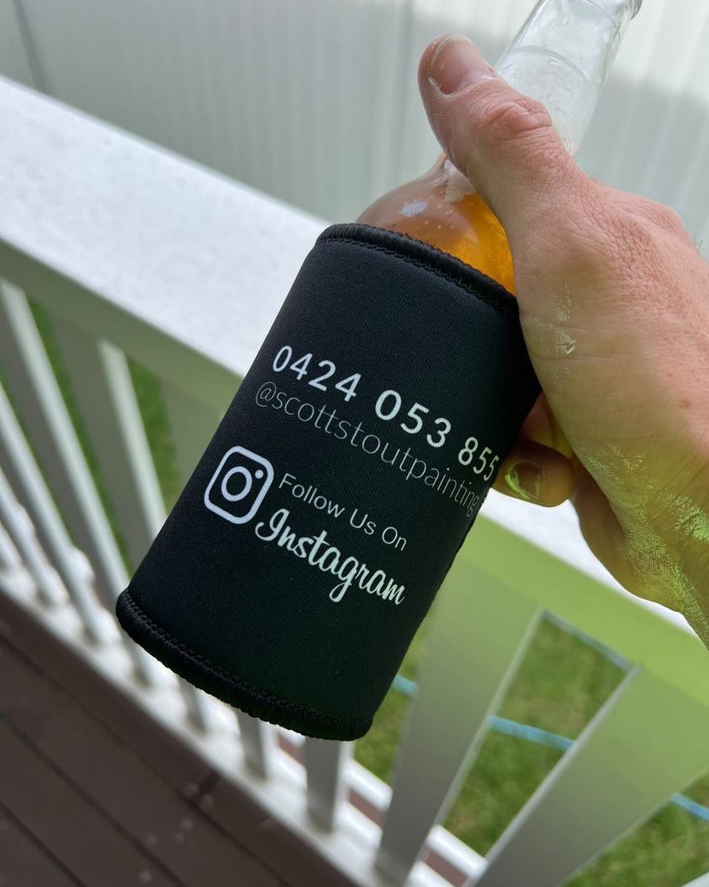 A person is holding a bottle of beer with a black sleeve that says follow us on instagram