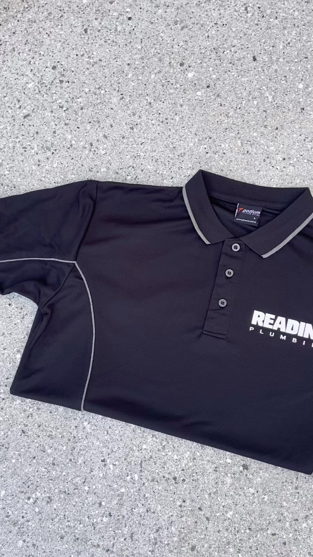 A black polo shirt is sitting on a gray surface.