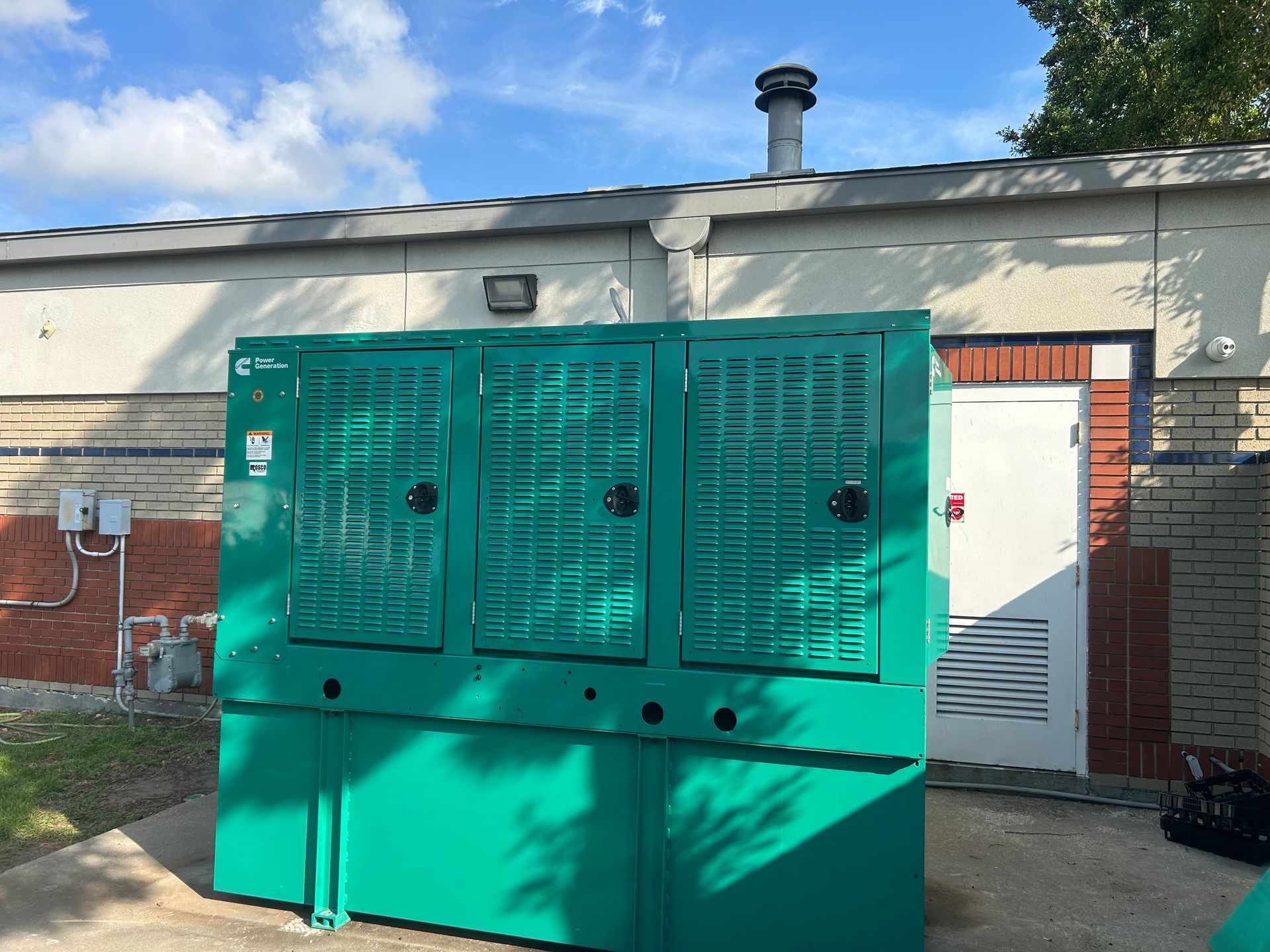 Green generator next to a building with a white door. Blue sky above.