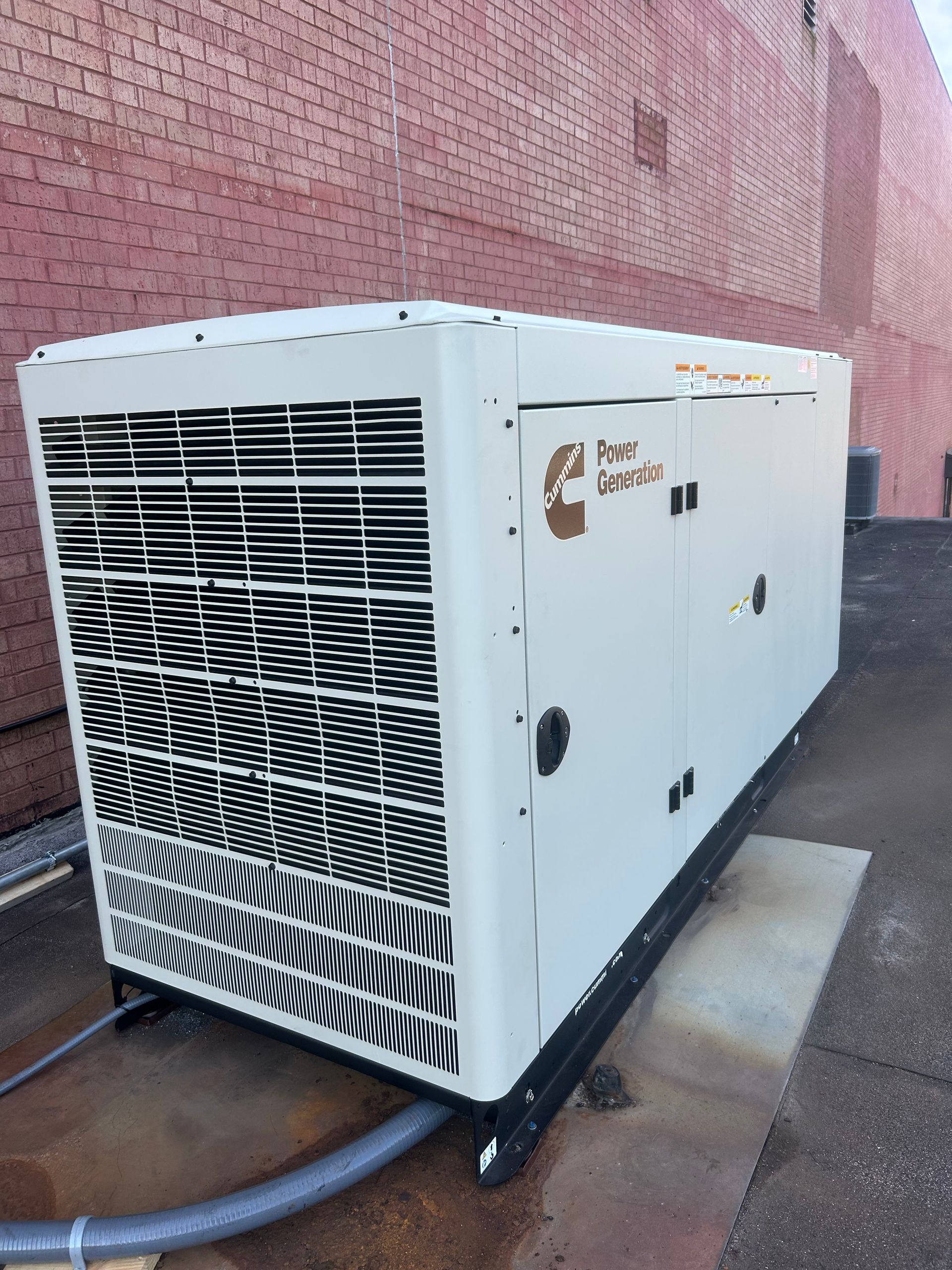 A large, beige Cummins generator sits next to a brick building.