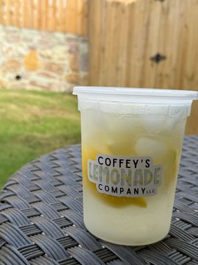 A cup of coffey 's lemonade company sits on a wicker table