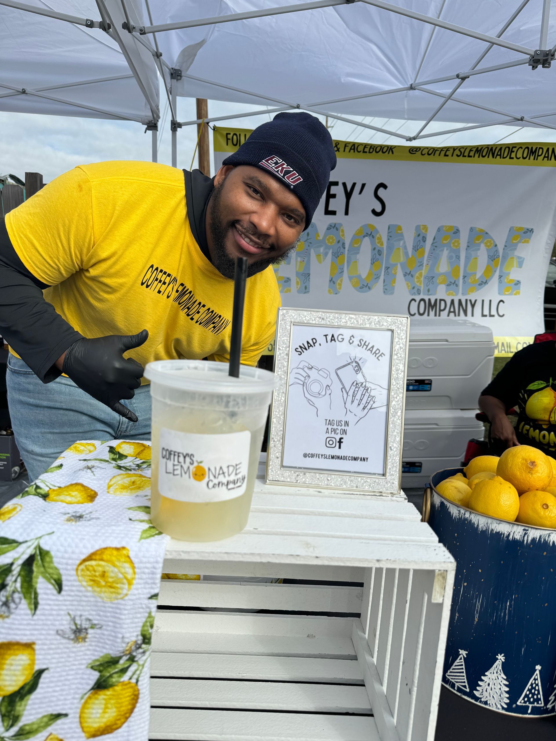 A man in a yellow shirt is selling lemonade at a market.